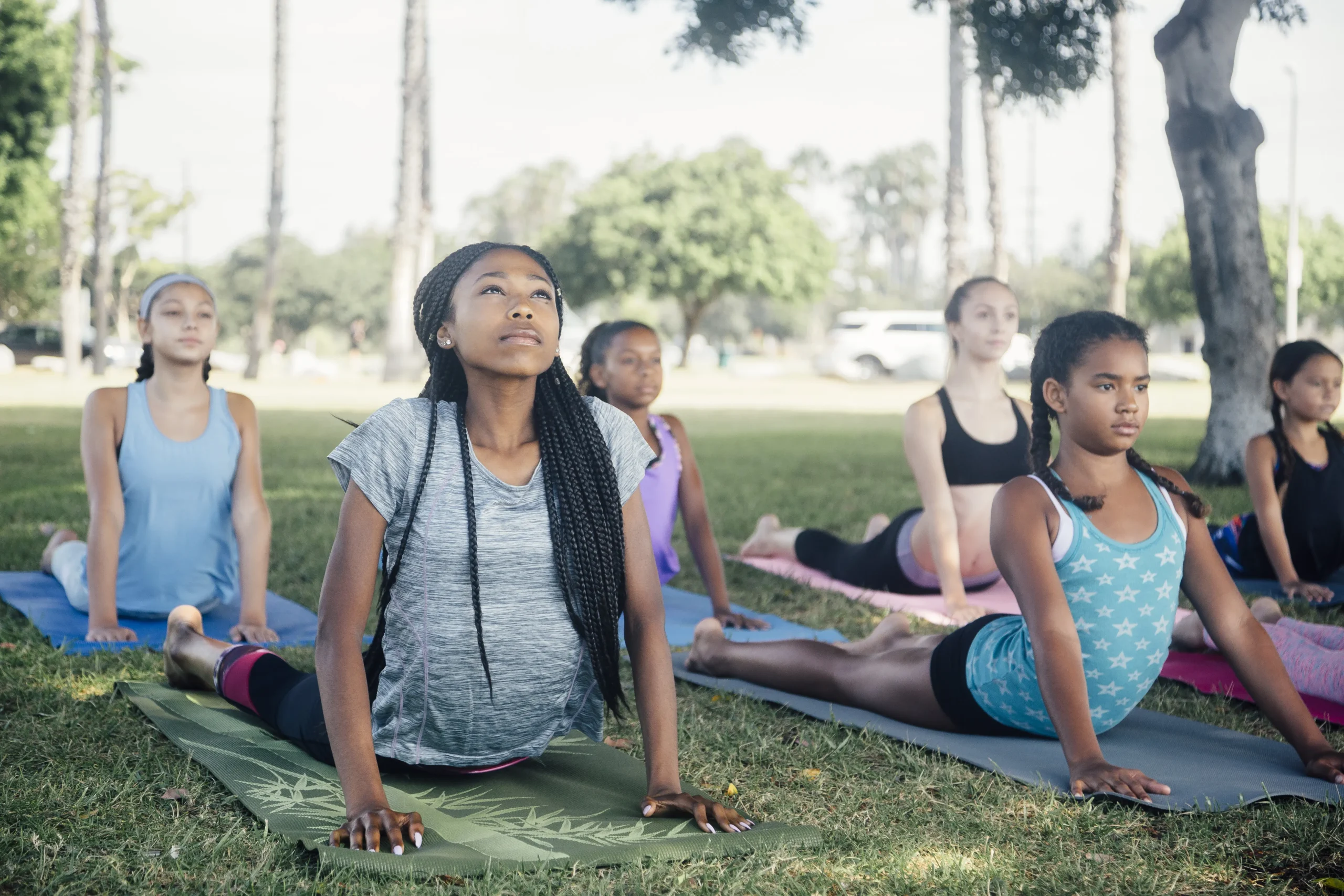 Teen girls practicing cobra pose outdoors during an ISHA WARRIORS yoga class to build strength and confidence.